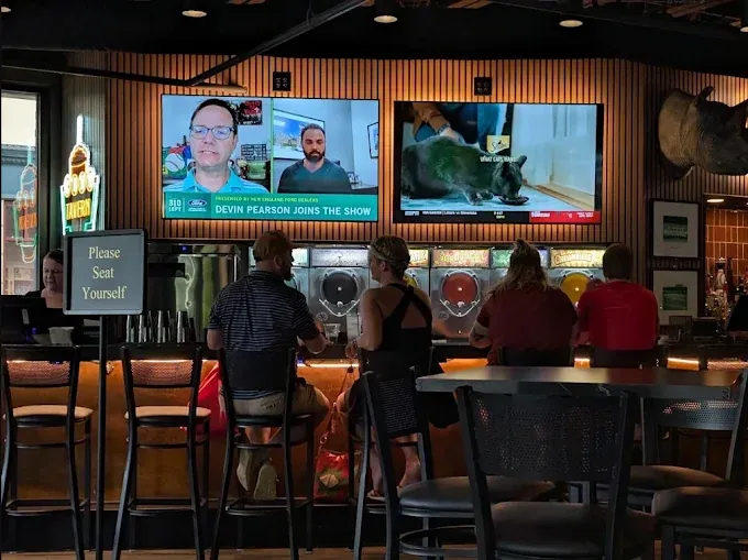 Restaurant bar and dining room with seating, a wood-slat wall and wall-mounted screens